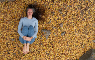 Woman doing a relaxation yoga pose lying on a ground of autumn leaves in nature view from above