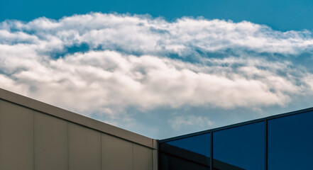 Fototapeta premium corner of a modern building with a window and a blue sky with clouds