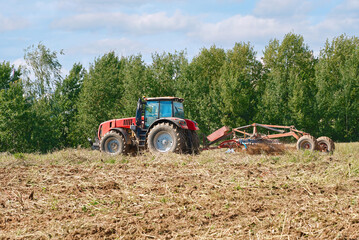 Tractor with plow attachment working the land in sprawling field, process of tillage in the farming cycle for crop production. Farming tractor in action, plowing rural field, soil preparation