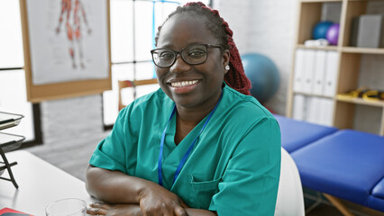African american woman with braids smiling in her workplace, a physiotherapy clinic interior,...