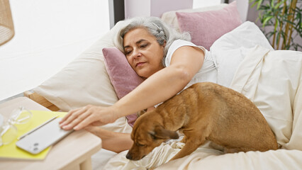 A mature woman relaxes in bed with her dog in a cozy home setting, evoking comfort, companionship,...