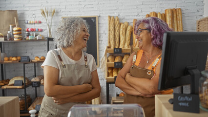 Women bakers laughing and standing with arms crossed in a bakery surrounded by bread and pastries