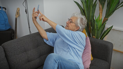 Senior woman takes a selfie on the couch in her cozy living room, embodying modern elderly lifestyle.