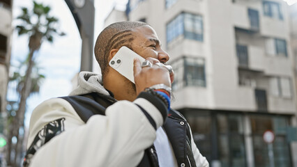 Fototapeta premium Handsome black man with beard talking on phone outdoors in urban city setting.