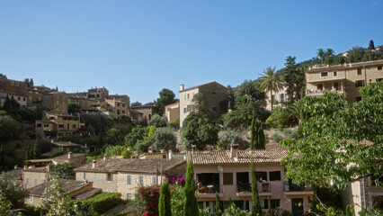 Obraz premium Mallorca village landscape with charming stone houses surrounded by lush greenery and perched on the rolling hills of deia under a clear blue sky.