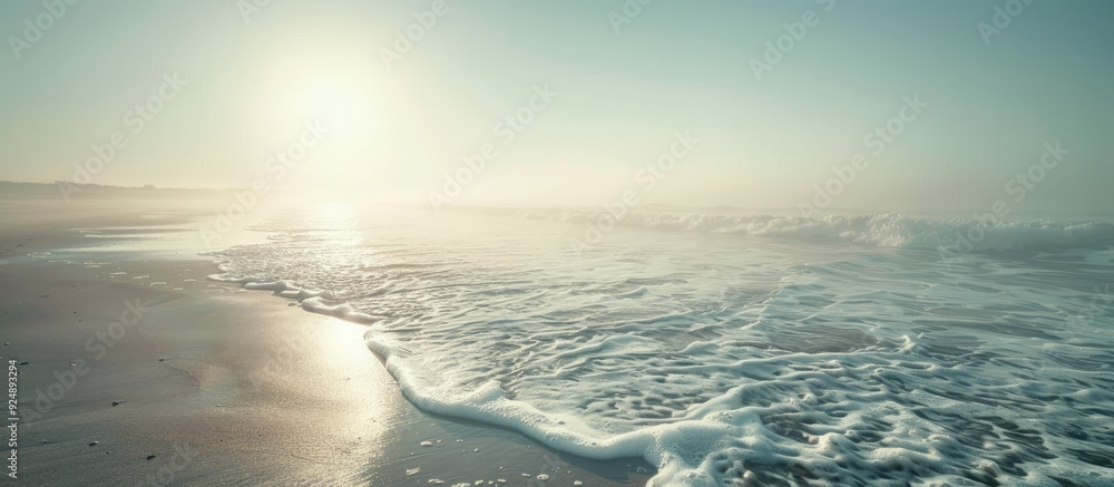 Poster misty morning sun shining above a sandy ocean shore with waves providing a clear view in the distanc