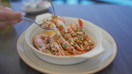 Close-up of a woman enjoying a gourmet shrimp plate with fork at a restaurant.