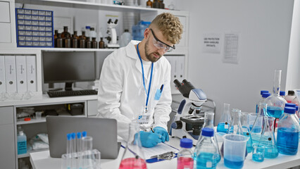 Fototapeta premium Bearded scientist in lab coat taking notes in modern laboratory with microscope and beakers
