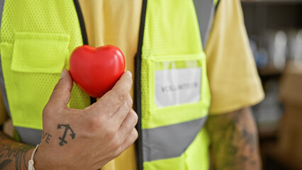 A man in a high-visibility vest holds a red heart, symbolizing care and safety at work.