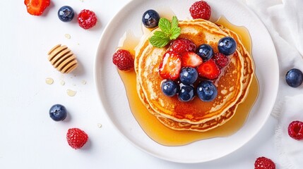 Whole-grain pancakes topped with fresh berries and a drizzle of honey. Top view on a white ceramic plate.