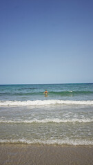 Obraz premium Woman swimming in the ocean with clear blue sky and waves crashing on the sandy shore, evoking a sense of summer and relaxation
