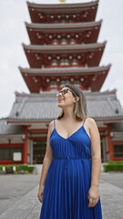 Cheerful, beautiful hispanic woman with glasses joyfully exploring and admiring the majestic senso-ji temple as she casually strolls, looking around with awe and a confident smile.