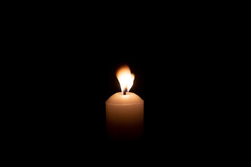 A single candle light glowing on a big white candle against blowing wind on table in church for Christmas, funeral or memorial service with copy space isolated on black background