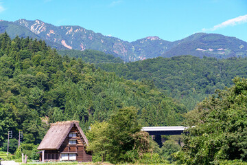 山の中の茅葺屋根の家と高速道路