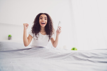 Photo of young attractive woman sit bed winning hold device excited wear stylish pajama soft comfy bedroom white room interior inside
