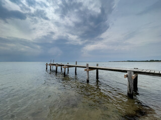 Obraz premium Rickety jetty jutting out from the beach under a threatening thunderstorm sky