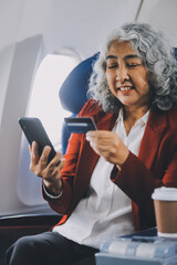 An adult woman sits by the window on a passenger plane, eagerly traveling abroad. She gazes at the...
