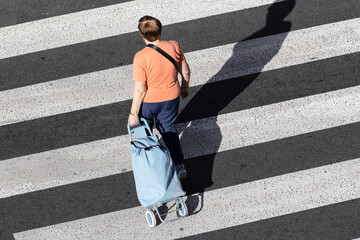Unrecognizable senior Woman pulling a grocery trolley across a crosswalk on a sunny day. High angle view