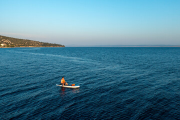 Man in orange vest navigating on the paddleboard in the sea at sunset.