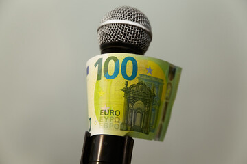 A 100 euro banknote wrapped around a microphone. The influence of money on public opinion, the...