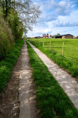 Chemin agricole goudronné le long d'une prairie et d'un corps de ferme