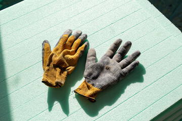  Dirty black work gloves on green thermal insulation boards background. Used construction work gloves.