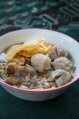 A bowl of Indonesian bakso, featuring meatballs, fried bakso, wontons, noodles, beef fat chunks, and savory broth. A hearty and flavorful dish.