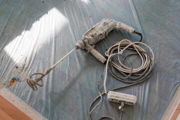 Large hammer drill with mixer bit, power cable and three-way socket. A blue plastic cleaning...
