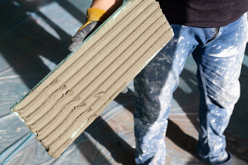 Construction worker bricklayer holds xps (Extruded Polystyrene) plate on which he applied mortar during interior heat and sound insulation project.
