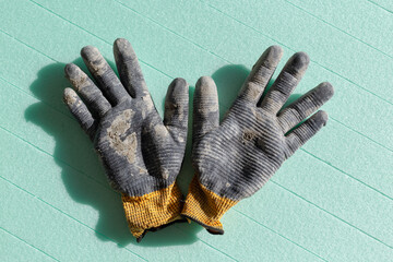 Used construction work gloves. Dirty black work gloves on green thermal insulation boards background.