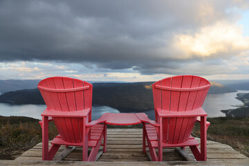 Two red adirondack chairs on a wooden deck overlooking Bonne Bay; Newfoundland and Labrador, Canada