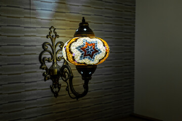 Wall sconce decorated with colored glass. Vivid glass lighting fixture. Classic sconce with turned on bulb under lampshade hanging on wall.