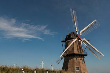 Tall windmill turbines against a clear blue sky, generating renewable energy in the serene Dutch landscape by the sea