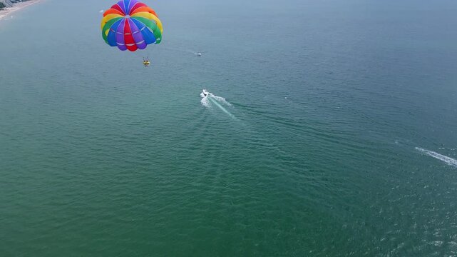 Drone video of a colorful parasail soaring over the open ocean, towed by a speedboat below. The aerial view captures the thrill and freedom of parasailing against a vast, serene seascape