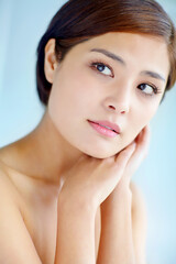 Fototapeta premium Asian woman, thinking and touch for skincare, dermatology and beauty in studio with healthy skin. Female person, vision and hygiene routine on blue background for facial treatment, self care and glow