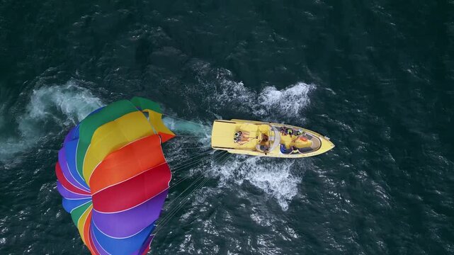 Drone video of a colorful parasail being towed by a speedboat over the ocean. The scene captures the excitement of parasailing with stunning views of the coastline and open sea