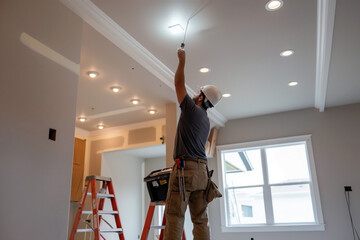 Electrician installing a new light fixture on the ceiling, with a toolbox and ladder in a modern living room.