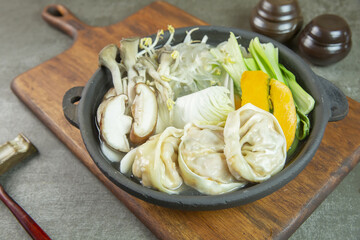 Close up of Korean food Dumpling Hotpot with sweet pumpkin, mushroom and bok choy on cast iron pan and wood cutting board, South Korea