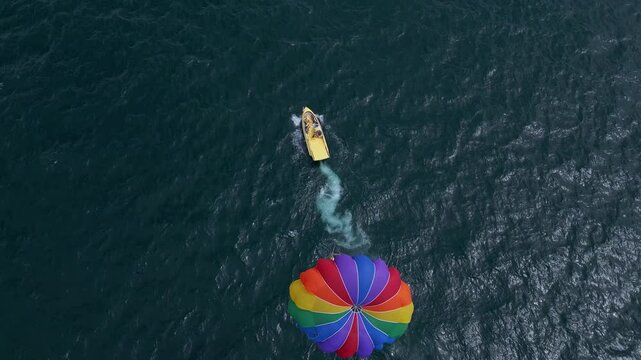 Drone video of a colorful parasail being towed by a speedboat over the ocean. The scene captures the excitement of parasailing with stunning views of the coastline and open sea