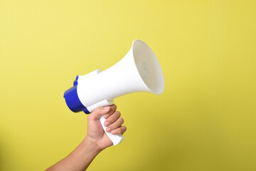 Close up hand holding megaphone isolated on yellow background. Concept of hiring, advertising something. Banner. Copy space