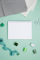 Composition with various threads and sewing accessories on green background. Mock up notebook