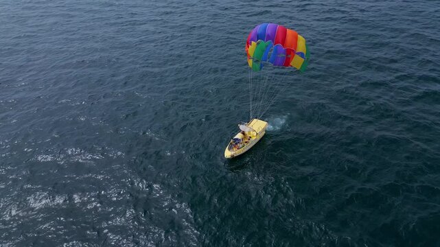 Drone video of a colorful parasail being towed by a speedboat over the ocean. The scene captures the excitement of parasailing with stunning views of the coastline and open sea