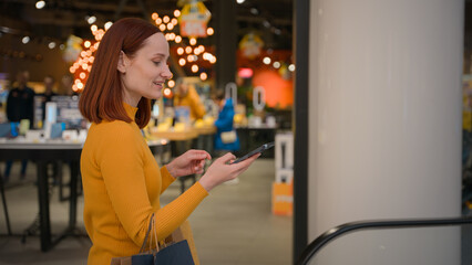 Smiling happy Caucasian woman female girl businesswoman shopper buyer customer client answering mobile phone smartphone call talking tell sales discount enjoy shopping rides escalator indoor shop mall
