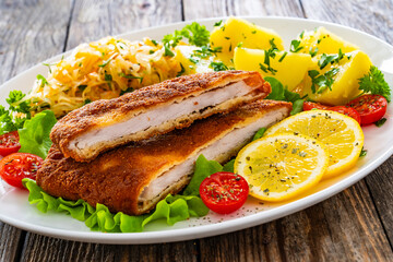 Crispy breaded fried pork chop, boiled potatoes and sauerkraut salad served on white plate on wooden table 