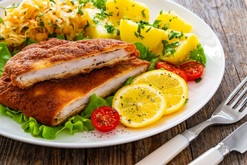 Crispy breaded fried pork chop, boiled potatoes and sauerkraut salad served on white plate on wooden table 
