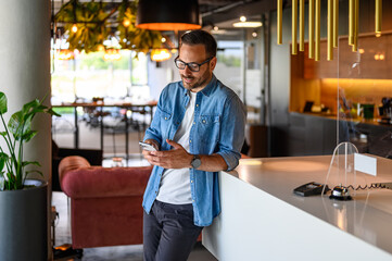 Serious young businessman checking social media applications over mobile phone by table in office