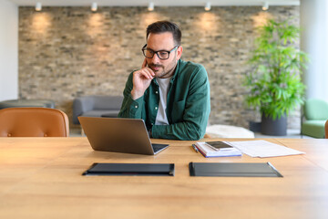 Fototapeta premium Portrait of confident web designer in glasses developing computer software at desk in modern office