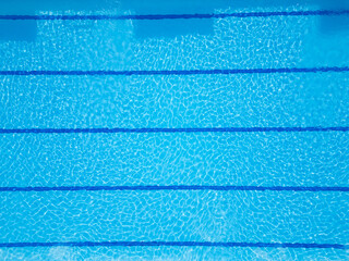 Drone video of a swimming pool with crystal-clear blue water and lane markings. The top-down view...