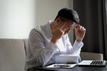 Young asian business man massaging rubbing stiff sore neck and headache tensed muscles fatigued...