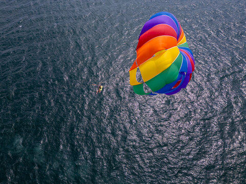 Drone video of a colorful parasail soaring over the open ocean, towed by a speedboat below. The aerial view captures the thrill and freedom of parasailing against a vast, serene seascape